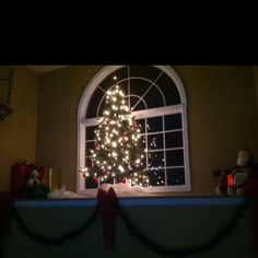 a christmas tree is lit up in front of a window with presents on the windowsill