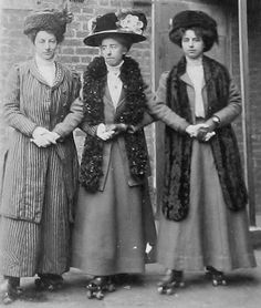 three women standing next to each other in front of a brick building