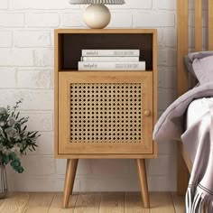 a bedside table with a lamp and books on it next to a bed in front of a brick wall