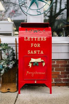 a red mailbox sitting on the side of a building next to a christmas wreath