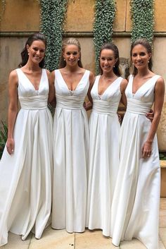 four bridesmaids in white dresses posing for the camera with greenery behind them