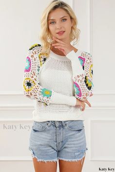 a beautiful young blond woman posing for the camera wearing shorts and a white sweater with colorful crochet sleeves