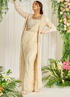 Featuring an ivory-hued shimmer georgette pre-draped saree paired with a U-neckline bustier detailed with pearl, bead, and sequin work. The look is finished with an embellished long cape featuring pearl tassels and a belt. This ensemble is a ready to wear saree for your ease ! Composition : Saree: Georgette, Blouse: Silk, Cape & Belt: Crepe Care: Dry Clean Only and Vacuum Storage All products can be customised for sleeves, length of blouse and neck design Delivery : 4-6 weeks as the product is hand crafted. Check Size Guide or choose MySize for free customisation (All Sizes above XL can be made at 15% additional cost) For more information and sizes please contact fabiliciousfashion@gmail.com or visit our Copenhagen studio. About the Designer : Nidhika Shekhar's label, founded in 2014, is a Cinderella Fashion, Saree Jacket, Maggam Designs, Embroidery Geometric, Jacket Designs, Embroidered Cape, Fancy Sarees Party Wear, Dress Book, Padded Blouse