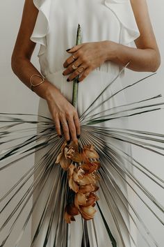 a woman in a white dress holding a bouquet of flowers and palm fronds