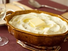 there is a bowl of mashed potatoes with butter on top and wine glasses in the background