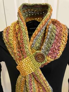 a multicolored crocheted scarf on a mannequin torso with a button in the center