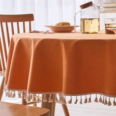 an orange table cloth with tassels and a bowl of food on it next to a wooden chair