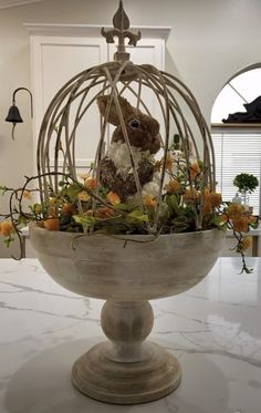 a white birdcage filled with flowers on top of a marble counter topped with a stuffed animal