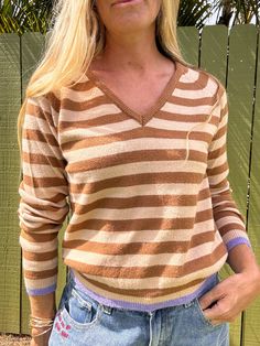 Stay stylish and cozy in our Emery striped sweater! This knitted top features a flattering V-neck, long sleeves, and a trendy striped pattern. Perfect for staying warm and looking chic. Why we love it: This sweater is nice and light weight with slight v neck that's not too low. The pop of purple on the cuff and hem is really fun and adds just little something special to this otherwise neutral stripe. Great for layering when traveling or throwing in your bag if you're worried about maybe getting Fall Striped Collar V-neck Top, Fall V-neck Top With Striped Collar, Knit Long Sleeve Tops With Striped Hem, Chic Long Sleeve Sweater With Contrast Stripes, Striped Fine Knit Long Sleeve Top, Striped V-neck Winter Sweater, Striped V-neck Sweater For Winter, Striped Long Sleeve Fine Knit Top, Casual Striped V-neck Sweater With Long Sleeves