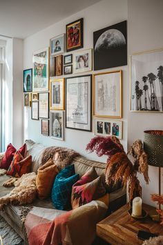 a living room filled with lots of pictures on the wall and couches covered in blankets