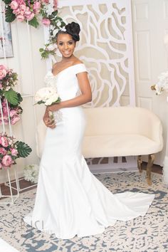 a woman in a white dress posing for the camera with flowers around her neck and hands behind her back