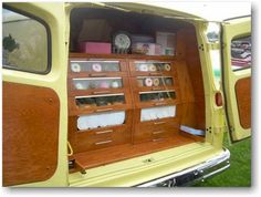 the back end of an old yellow truck with its doors open and shelves full of donuts