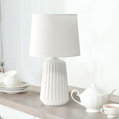 a white lamp sitting on top of a table next to a cup and saucer