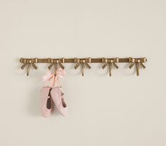 a pair of ballet shoes hanging on a wall with gold hooks and bows attached to it