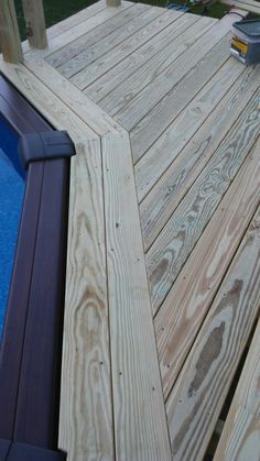 a wooden deck next to a pool with a trash can on the ground near it