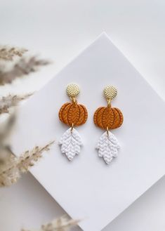 an image of a pair of earrings on top of a white surface with dried grass