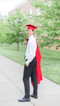 a man in a red cap and gown is standing on the sidewalk with his graduation robe draped over his shoulders