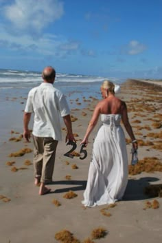 a bride and groom walking on the beach with seaweed all around them, holding hands