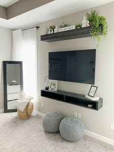 a flat screen tv sitting on top of a wooden shelf in a living room next to a window