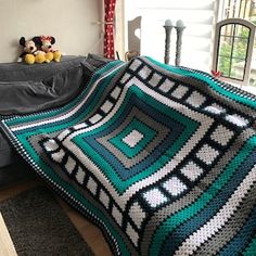 a crocheted blanket is sitting on a couch next to a teddy bear and window