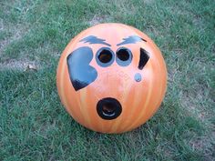 an orange bowling ball with holes painted on it's face sitting in the grass