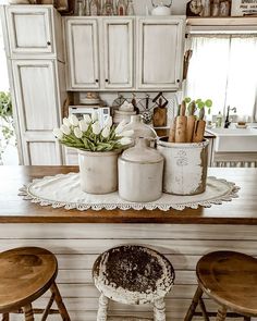 an old fashioned kitchen with white cabinets and wooden stools in front of the counter