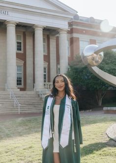 a woman standing in front of a building wearing a green graduation robe and white dress