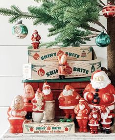 santa clause figurines and other christmas decorations on a mantel in front of a pine tree