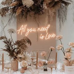 a table topped with lots of vases filled with flowers next to a neon sign that says will you marry me?