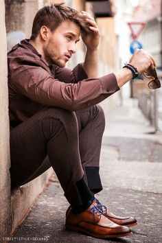 a man sitting on the side of a building next to a wall with his hand on his head