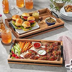 two trays filled with food sitting on top of a table next to plates and glasses