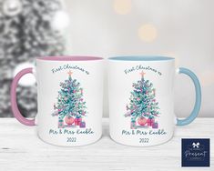 two coffee mugs with christmas trees on them, one is pink and the other is blue