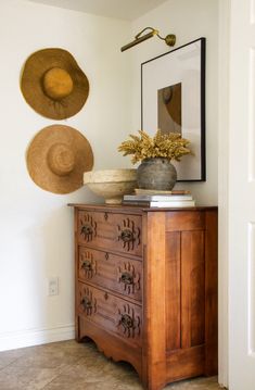 two hats are hanging on the wall next to a dresser with an old fashioned chest