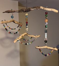 three pieces of driftwood are hanging from the ceiling with beaded necklaces on them