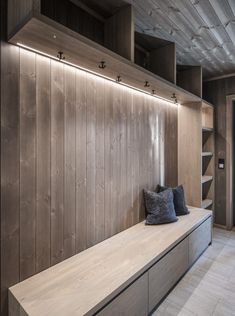 a wooden bench with two pillows on it in front of a book shelf and bookshelf