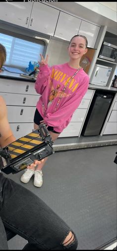 two people in a kitchen one holding a skateboard and the other pointing at something