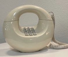 an old fashioned phone sitting on top of a white table next to a gray wall