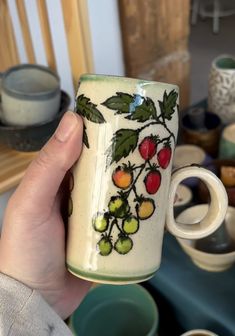 a hand holding a coffee cup with fruit painted on it