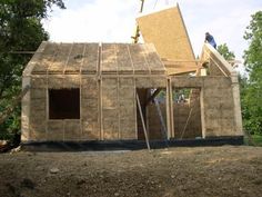 a man standing on top of a roof next to a house under construction in the woods