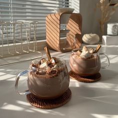 two mugs filled with hot chocolate and marshmallows on top of a table