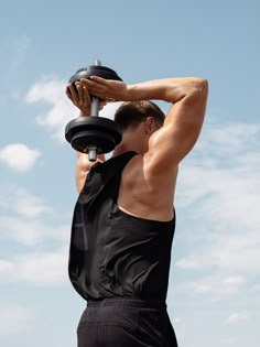 a man is doing exercises with his dumbbells in front of the blue sky