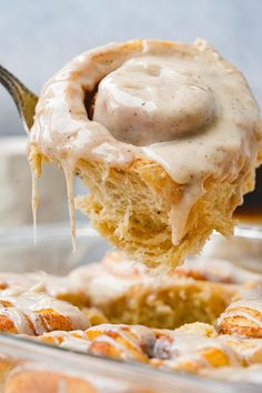 a spoonful of cinnamon roll with icing on it is being held by someone