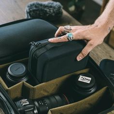 a person's hand on top of a camera bag with other items in it