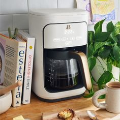 a green coffee maker sitting on top of a wooden cutting board next to a book