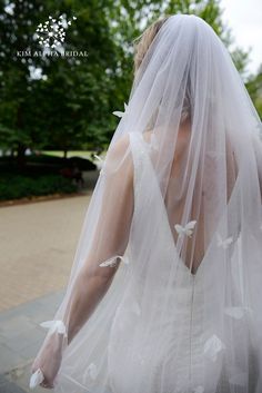 the back of a bride's wedding dress with white butterflies on it and her veil blowing in the wind