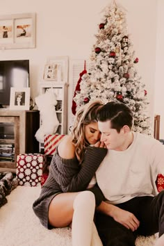 a man and woman sitting on the floor in front of a christmas tree