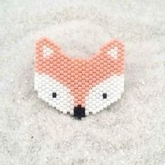 an orange and white beaded fox brooch sitting on top of snow covered ground