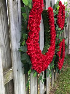 the letter o is made out of red flowers and greenery next to a wooden fence