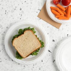 there is a sandwich and carrots in the bowl on the table next to each other