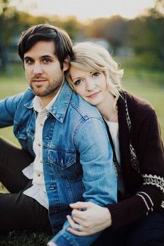 a man and woman are sitting on the grass in an open field, posing for a photo